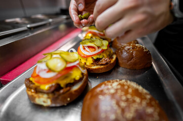 A chef assembles gourmet cheeseburgers with fresh ingredients—pickles, onions, tomatoes, melted...