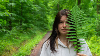 A young woman in a light beige hoodie holding a fern branch in the forest