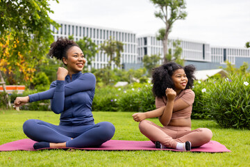 African American woman and her daughter in yoga suit are relaxingly practicing healthy stretching exercise together in the park for stiff muscle and preventing office syndrome