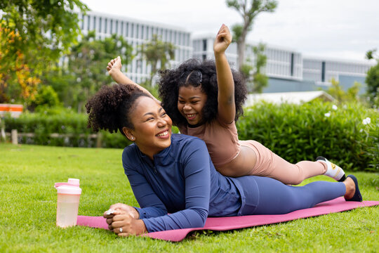African American mother and young daughter are lying down and playing ride after having yoga exercise public park for weekend leisure and happiness - Powered by Adobe