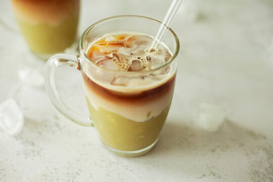 Trendy pistachio iced latte in a clear glass, on a white background with copy space &ndash; minimalist and refreshing aesthetic