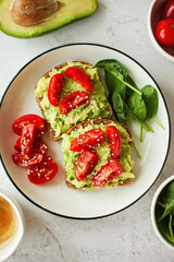 Vegan avocado sandwich, wholewheat bread stacked with creamy avocado and juicy cherry tomatoes and fresh spinach leaves - the perfect bite for a healthy, plant-based lifestyle