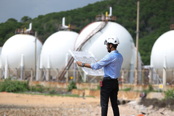 Industrial Chief engineer with safety PPE work with walkie talkie and drawing at front Refinery and gas petrochemical plant