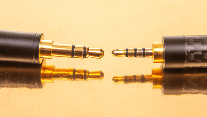 Close-up of two 3.5mm audio jacks with gold connectors on a reflective golden surface, ideal for tech and audio equipment themes