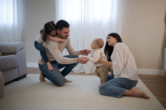 Happy family playing with baby learning to walk at home - Powered by Adobe