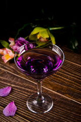 Cold purple violet exotic cocktail in glass with decorated flowers and petals. Tropical vibes.