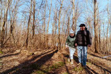Obraz premium An elderly couple, a man and a woman, walk through a spring forest, enjoying the beauty of nature. Sunlight filters through fresh green leaves, creating a serene and romantic atmosphere