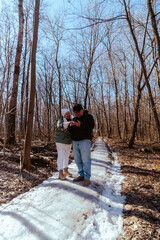 An elderly couple, a man and a woman, walk through a spring forest, enjoying the beauty of nature. Sunlight filters through fresh green leaves, creating a serene and romantic atmosphere