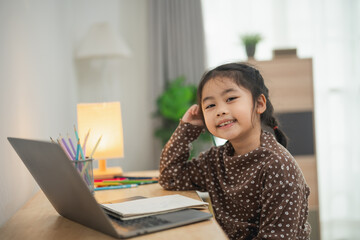 Fototapeta premium Happy young girl sitting at a desk with a laptop, smiling and enjoying her study time in a bright, cozy room, surrounded by stationery and plants