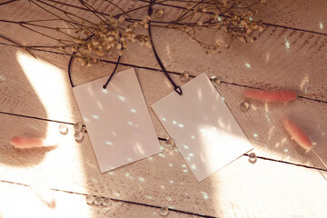 Two shapes of blank white paper label or cloth tag on wooden background with flowers, sparkles and sunlight, Price tag mockup template with copy space for brand, information. Shopping, sale concept