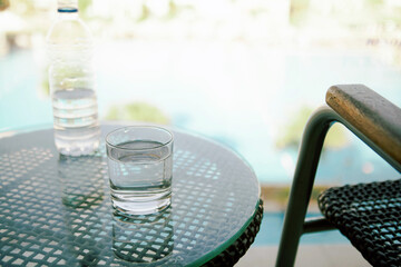 Glass with clear water and the half empty bottle on the coffee table in balcony in summer day. Space for text