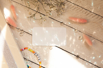 Copy space on white blank of card or business card on wooden background, decorating with necklace, flowers, sparkles and sunlight. Book, literature, paper, writing, texture and materials concept. 