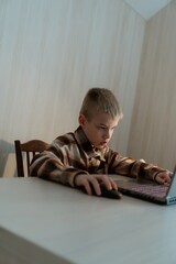 Fototapeta premium An 8-year-old boy joyfully plays computer games on his laptop at home. His face lights up with excitement as he enjoys the virtual adventure. A fun and engaging moment of childhood and technology
