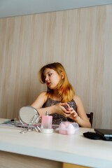A 13-year-old teenage girl is applying makeup and taking care of her skin in front of a mirror. She enjoys experimenting with beauty products, learning self-care, and developing her personal style