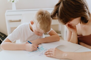 A loving mother and her son work together on homework at the kitchen table, symbolizing family...