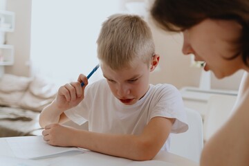 Naklejka premium A loving mother and her son work together on homework at the kitchen table, symbolizing family support, education, and care. The scene highlights the importance of parental guidance