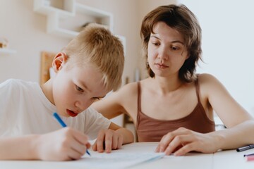 A loving mother and her son work together on homework at the kitchen table, symbolizing family...