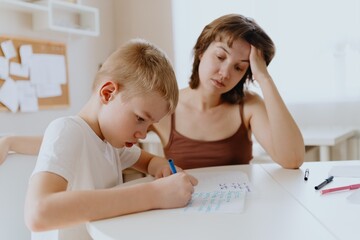 A loving mother and her son work together on homework at the kitchen table, symbolizing family...