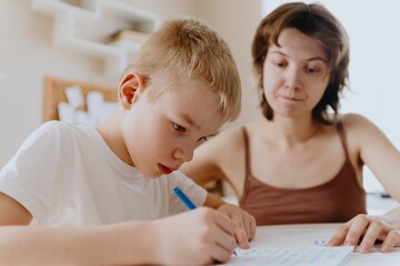 A loving mother and her son work together on homework at the kitchen table, symbolizing family...