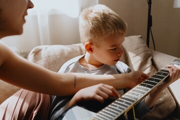 Mother and son playing guitar together, family love. The child wears a hearing aid, highlighting...