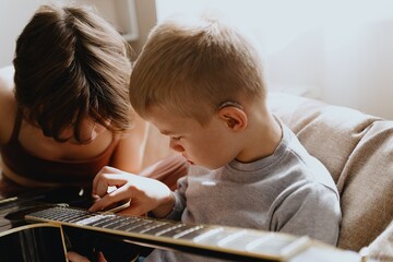 Mother and son playing guitar together, family love. The child wears a hearing aid, highlighting...