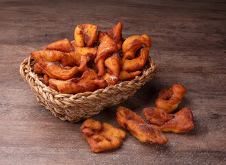 Traditional Crostoli Pastries in a Wicker Basket on Rustic Wooden Table, talian treats are sprinkled with sugar and arranged in an inviting, homemade style. Brazilian food.