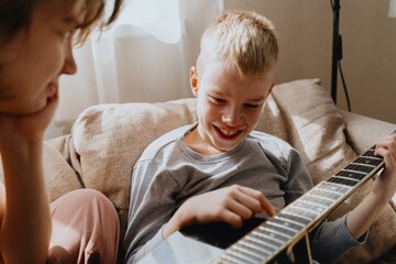 Mother and son playing guitar together, family love. The child wears a hearing aid, highlighting...