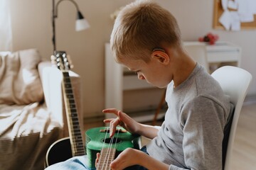 Mother and son playing guitar together, family love. The child wears a hearing aid, highlighting...