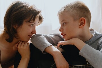 Mother and son playing guitar together, family love. The child wears a hearing aid, highlighting...