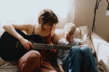 Mother and son playing guitar together, family love. The child wears a hearing aid, highlighting...