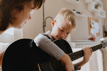 Mother and son playing guitar together, family love. The child wears a hearing aid, highlighting...