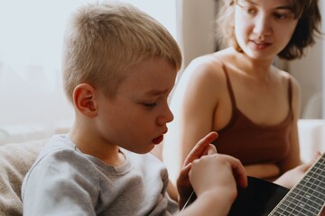 Mother and son playing guitar together, family love. The child wears a hearing aid, highlighting...