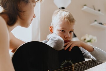 Mother and son playing guitar together, family love. The child wears a hearing aid, highlighting...