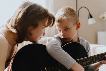 Mother and son playing guitar together, family love. The child wears a hearing aid, highlighting...