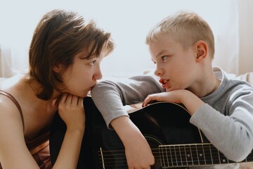 Mother and son playing guitar together, family love. The child wears a hearing aid, highlighting...