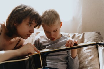 Mother and son playing guitar together, family love. The child wears a hearing aid, highlighting...