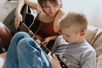 Mother and son playing guitar together, family love. The child wears a hearing aid, highlighting...