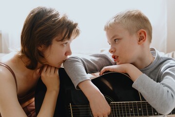 Mother and son playing guitar together, family love. The child wears a hearing aid, highlighting...