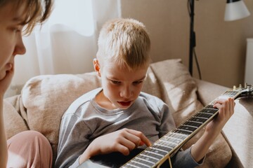 Mother and son playing guitar together, family love. The child wears a hearing aid, highlighting...