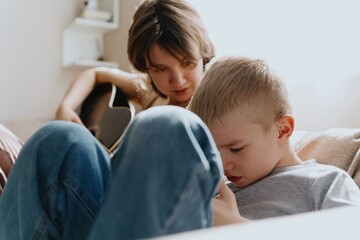 Mother and son playing guitar together, family love. The child wears a hearing aid, highlighting...