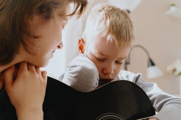 Mother and son playing guitar together, family love. The child wears a hearing aid, highlighting...