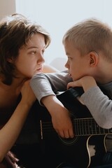 Mother and son playing guitar together, family love. The child wears a hearing aid, highlighting inclusivity and the universal language of music. Authentic, unedited photo captures emotions
