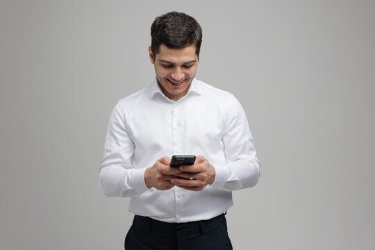 Man in white shirt smiling while using smartphone in a modern indoor environment