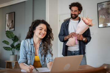Man surprising his working girlfriend with flowers at home