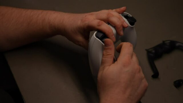 Closeup of technician hands disassembling wireless gaming controller sitting at table in workshop. Master repairing broken joystick on workbench, using screwdriver. Shooting in slow motion.