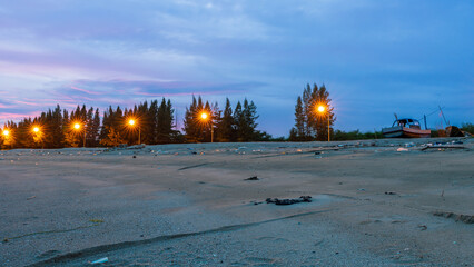 Photo of a beach full of trash in the evening with a beautiful red sky and clouds and sparkling lights illuminating the night street.