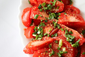 Fresh tomato salad closeup. Sliced tomatoes with chopped green onion. Simple homemade healthy meal. Light natural background. Summer vegetable food. Clean eating concept. Minimal white plate.