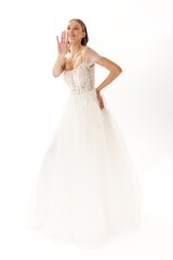 Young woman in elegant wedding dress poses gracefully against bright backdrop in indoor studio