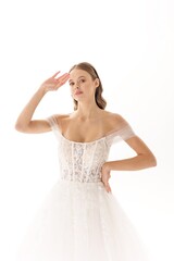 Elegant bride posing in white wedding dress with sheer sleeves against a plain background