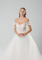 Elegant model showcasing a stunning white wedding dress with intricate lace details in a minimalist studio setting